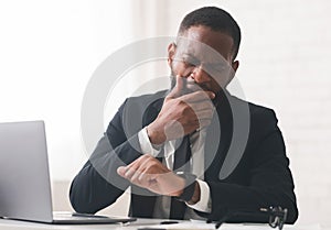 Tired manager checking time and yawning at workplace