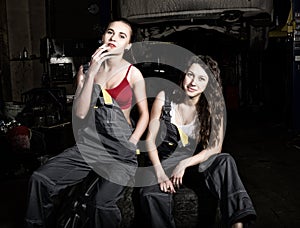 Tired mechanics girls sitting on a pile of tires on a car repairs, one of the girls smoke. colorless life concept