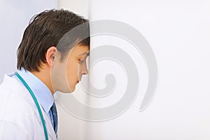 Tired medical doctor leaned his head into a wall