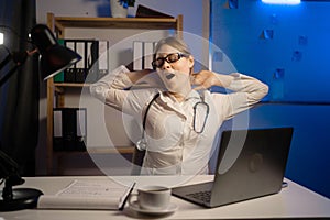 Tired medical doctor woman yawning in office duty at night.