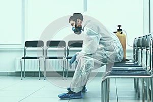 tired medical orderly in a protective suit sitting in a public waiting room.