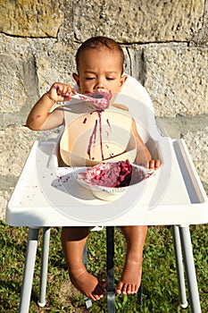 Tired messy baby boy eating blueberry cake with spoon