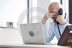 Tired mid adult businessman using telephone at desk in office