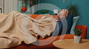 Tired middle-aged mature man lying down in bed taking a rest at home, napping falling asleep on sofa