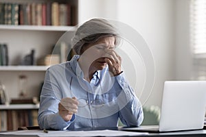 Tired middle aged woman taking off eyeglasses, suffering from pain.