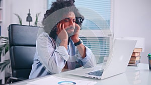 Tired Middle Eastern man clutches his head while sitting in his office