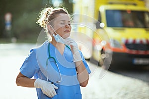 Tired modern paramedic woman breathing outside near ambulance