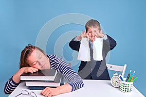 Tired mom of naughty boy schoolboy sleeping at school desk, blue background