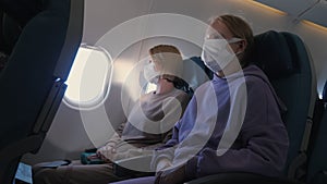 Tired mother and daughter fly on a plane. They are wearing protective masks. Traveling during the coronavirus pandemic