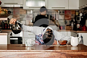 Tired mother, trying to pour coffee in the morning. Woman lying on kitchen table after sleepless night