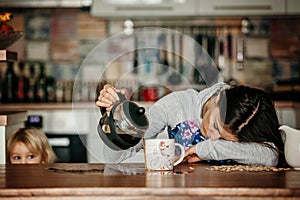 Tired mother, trying to pour coffee in the morning. Woman lying on kitchen table after sleepless night