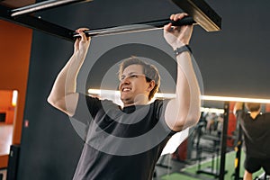 Tired motivated beginner sportsman showing hard expression on face in pulling up own body. Exhausted muscular male jumps