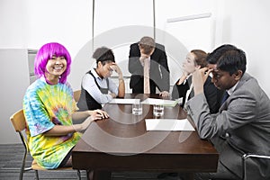 Tired multiethnic businesspeople with colleague in pink wig at meeting