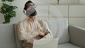 Tired muslim man take break laptop work at home wear headphones listen relaxing music. Exhausted businessman in headset