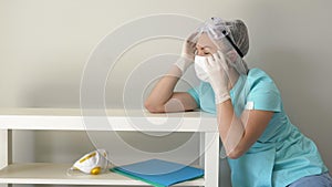 Tired nurse is sitting on the floor after a long day at the hospital. She takes off her face mask and goggles. Covid-19.