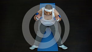 Tired obese male doing dumbbells exercise at home, ineffective training program