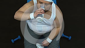 Tired obese man wiping sweat with towel and drinking water after sport workout