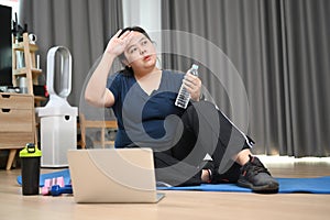 Tired obese woman sitting and resting after doing fitness exercises at home.