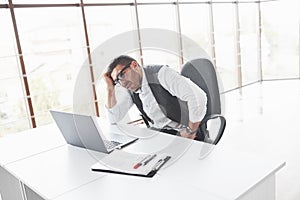 Tired office worker sitting in the spacey room and looking at his laptop