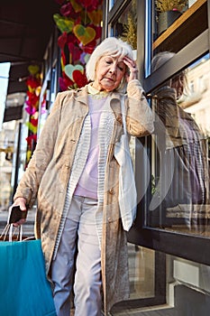 Tired old age female wearing coat with multicolor shopping bags