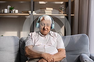 Tired old man listening to music from big wireless headphones
