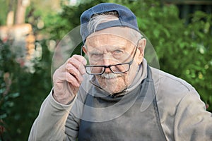 Tired old man looks at his interlocutor, adjusts his glasses. The old man can`t see very well without his glasses photo