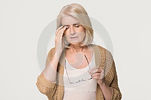 Tired old woman holding glasses feeling eyestrain on background