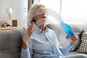 Tired older woman waving fan, suffering from heat at home