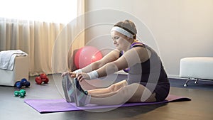 Tired overweight girl trying to reach toes with great effort, stretching workout