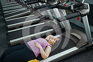 Tired overweight woman lying on treadmill in gym