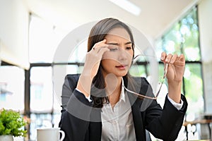 Tired and overworked Asian businesswoman taking off her eyeglasses while working at her desk