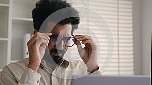 Tired overworked man Indian Arabian businessman working on laptop in glasses confused business employer taking off