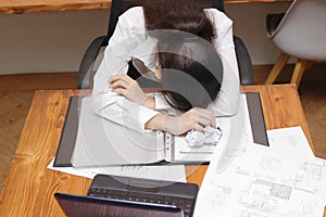 Tired overworked young Asian business woman bend down head on workplace in office.