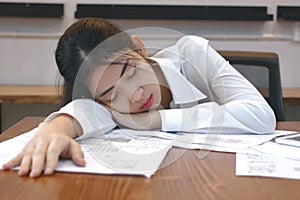 Tired overworked young Asian business woman lying down on the desk in office.