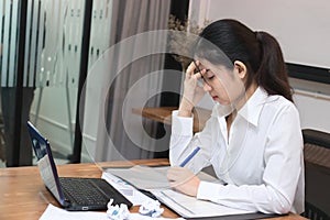 Tired overworked young Asian business woman suffering from severe depression in workplace of office