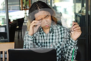 Tired overworked young Asian man with laptop being overloaded in office.