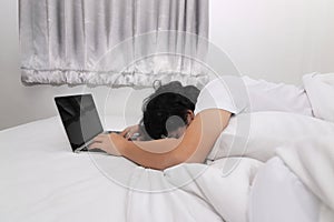 Tired overworked young Asian man with laptop sleeping on the white bed in bedroom. Work from home and quarantine concept