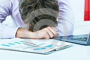 Tired overworked young businessman sleeping over a laptop in a desk at job in his office.