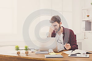 Tired, overworking businessman with laptop in modern white office