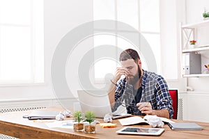 Tired, overworking businessman with laptop in modern white office