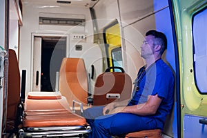 Tired paramedic on duty, sitting in an ambulance car, waiting for the next call