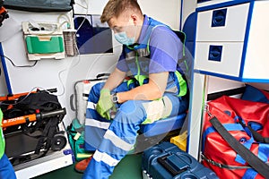 Tired paramedic in a protective mask sits in an ambulance