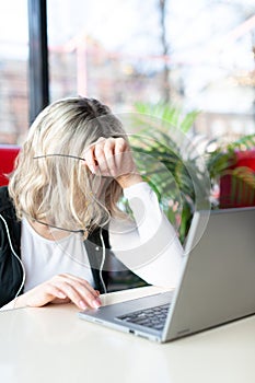 Tired person at the laptop. Woman sits in a cafe and works online, she lowered her head and holds her glasses in hand