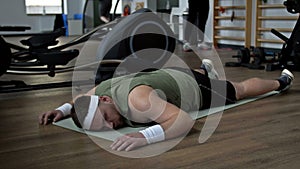 Tired from physical activity, a young overweight man lies prone on a karemat in the gym.