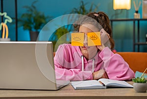 Tired preteen school girl sleeping on laptop computer with eyes stickers on face, cheating to sleep