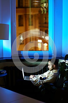 Tired programmer in dark office work on laptop. Workaholic businessman typing on computer at night