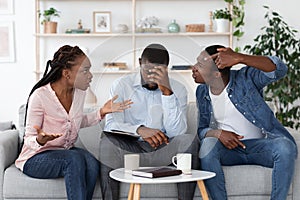 Tired Psychotherapist Sitting On Couch Between Quarreling Couple During Therapy Session