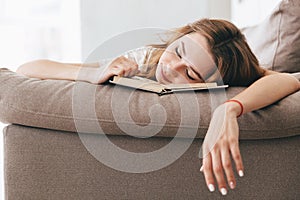 Tired relaxed woman sleep with book on sofa