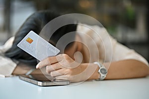 Tired and sad Asian woman laid her head down on the table, holding a credit card