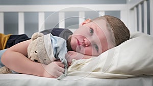 Tired and sad child due to problems in family is sad lying on bed alone hugging his best friend teddy bear. Problems of